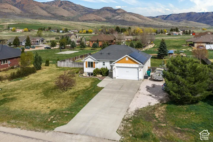 Single-story residence featuring a concrete driveway, two-car garage, roof-mounted solar panels, wood-composite siding, and a mountain backdrop
