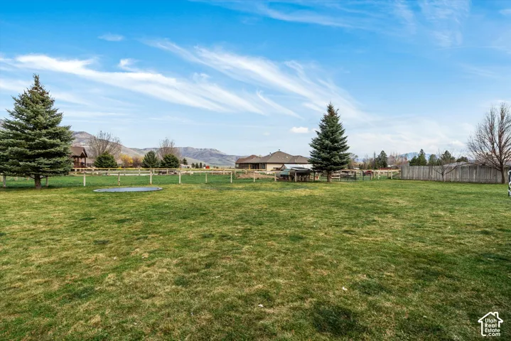 Expansive grass lawn featuring mature evergreen trees, post-and-rail perimeter fencing, and a backdrop of mountain terrain