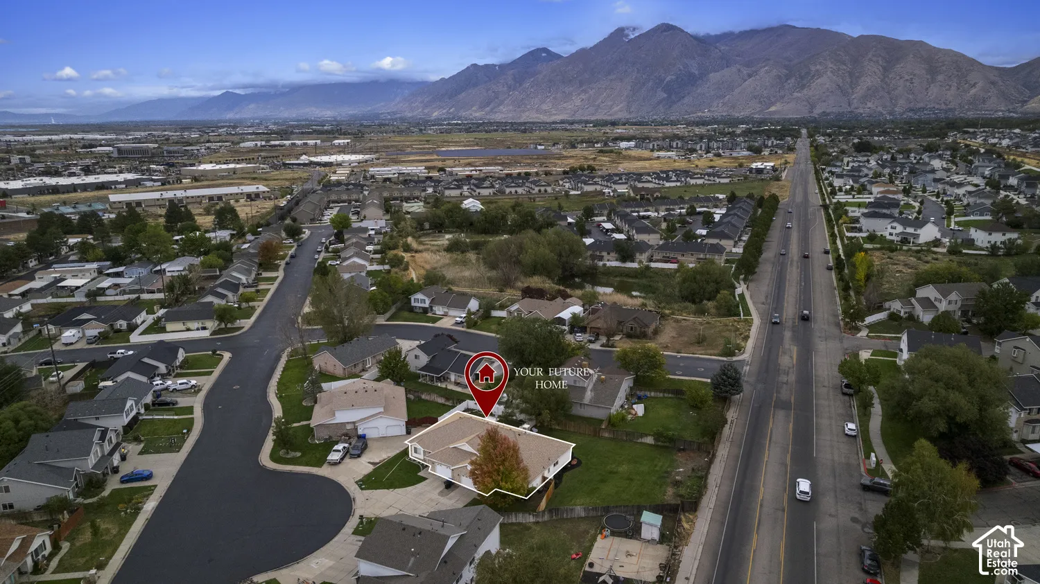Aerial perspective featuring a single-story residence with a multi-gabled roof, integrated garage, and fenced backyard, situated against a backdrop of mountain scenery