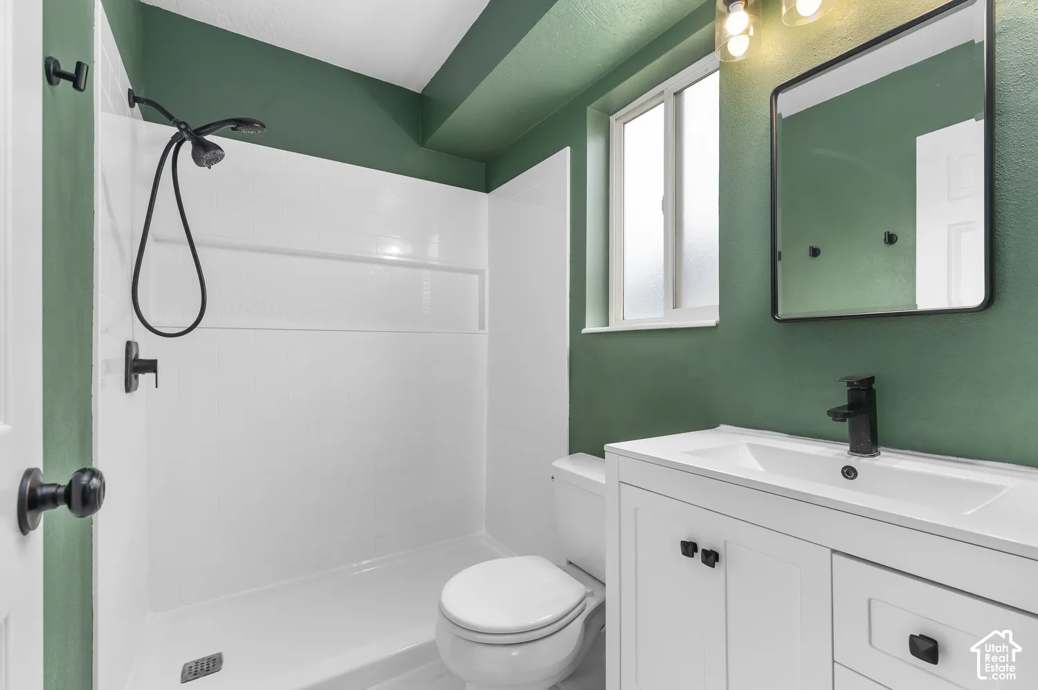 Bathroom featuring a white vanity cabinet with a integrated sink, matte black faucet, wall-mounted mirror with black trim, and shower stall with a handheld showerhead