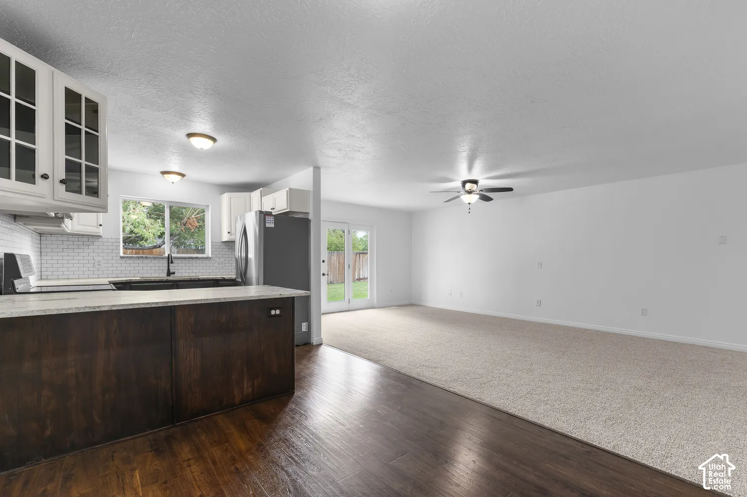 Kitchen featuring a stone-topped island, dark wood-finish cabinetry, white tiled backsplash, ceiling-mounted light fixtures, and glass-paneled double doors