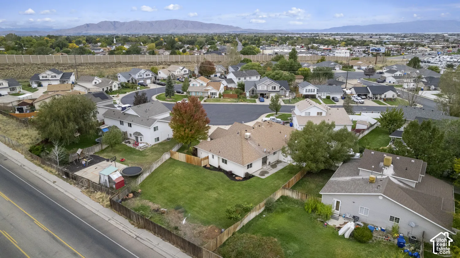 Aerial perspective of a residential property featuring a fenced backyard, manicured lawn, mature trees, and a mountain range backdrop