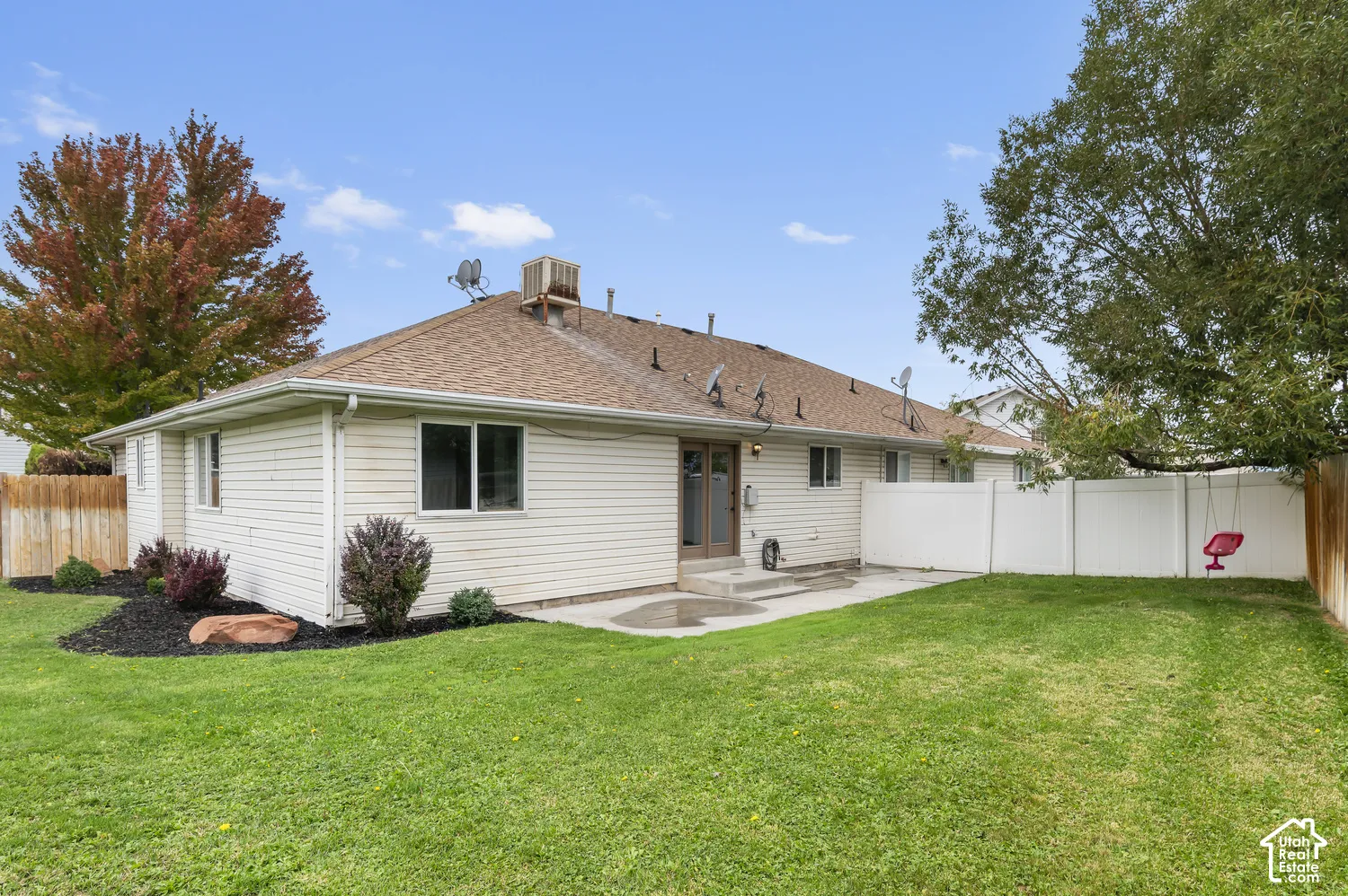 Exterior elevation featuring light-toned horizontal siding, a composition shingle roof, a concrete patio, and white vinyl perimeter fencing
