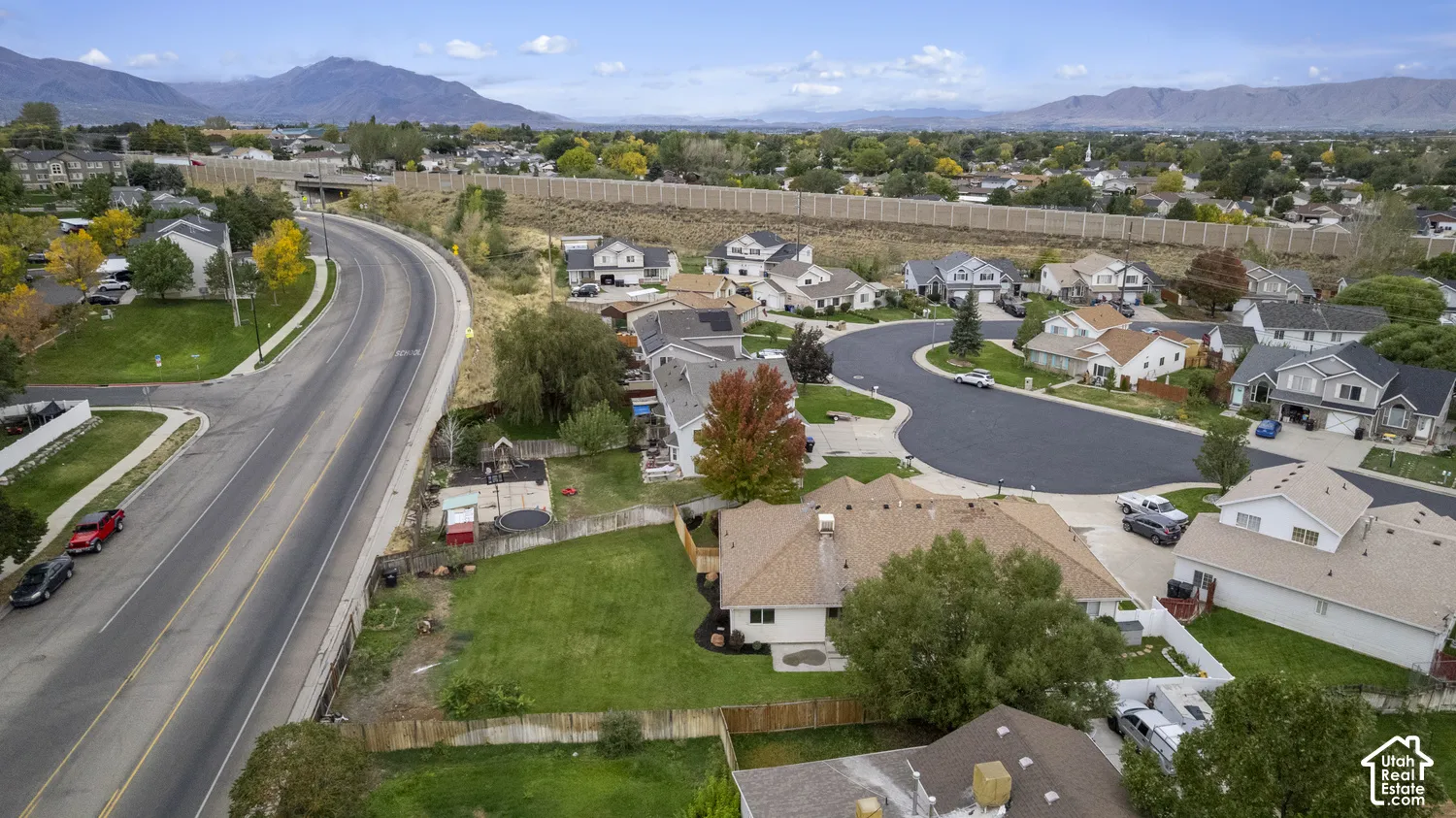 Aerial perspective of a residential property featuring an expansive grass lawn, wood-panel fencing, a multi-pitch shingled roof, and a mountain backdrop