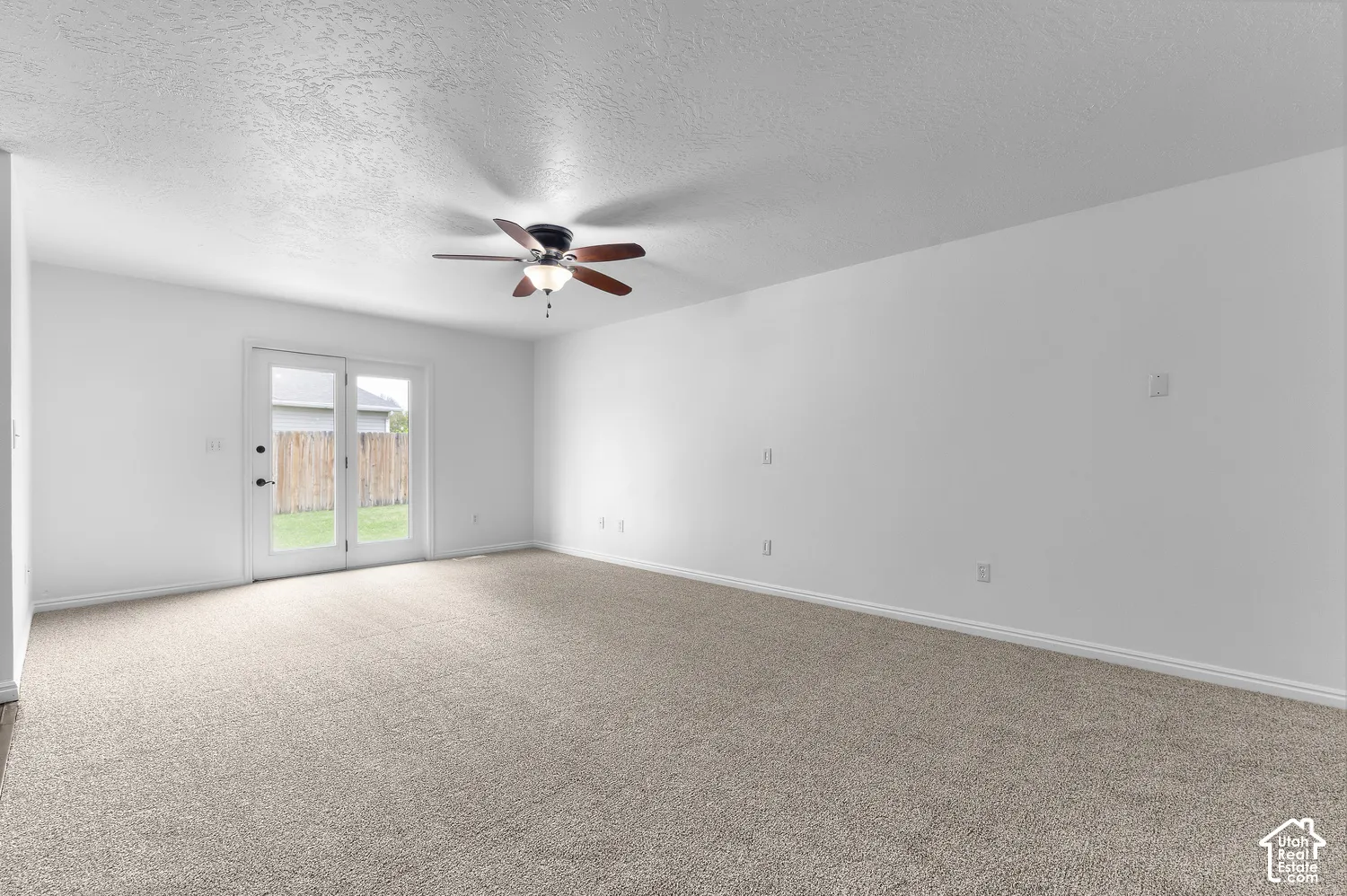 Neutral-toned carpeting, ceiling fan with integrated light fixture, and glass-paneled double doors leading to the exterior