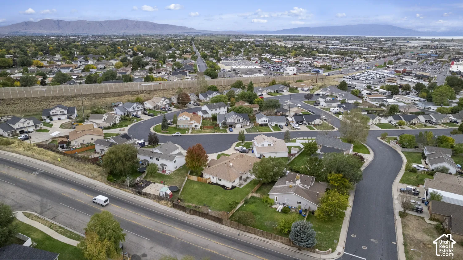 Aerial perspective of the residential area featuring asphalt streets, manicured green space, mature trees, and a mountain range backdrop