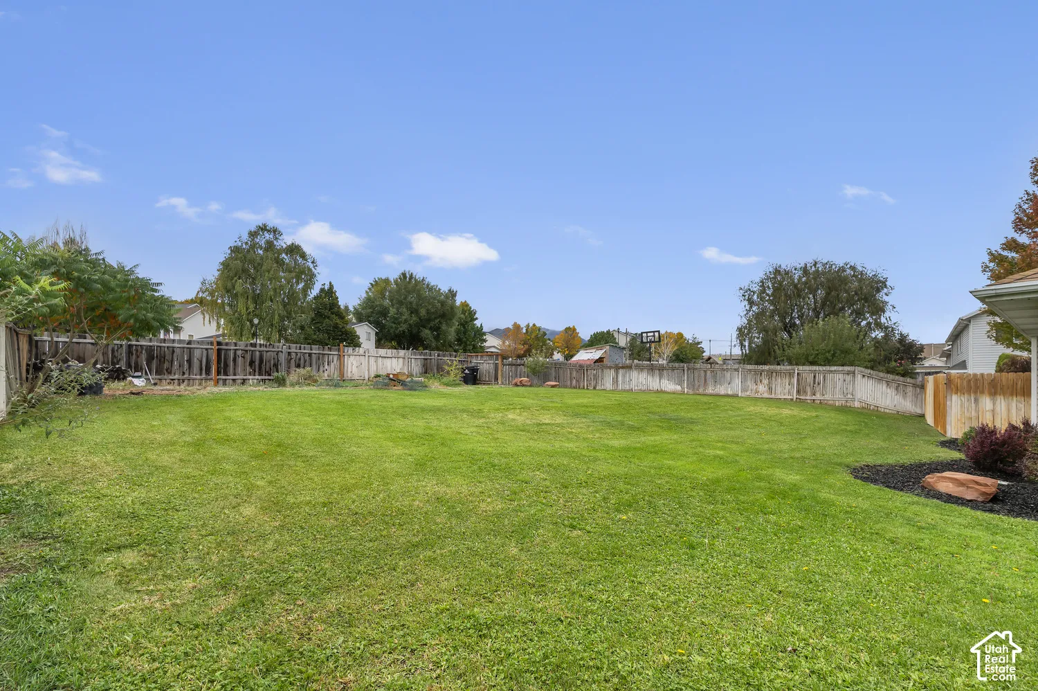 Expansive backyard featuring a large grass lawn, full-perimeter wood fencing, and landscaped garden beds with stone accents