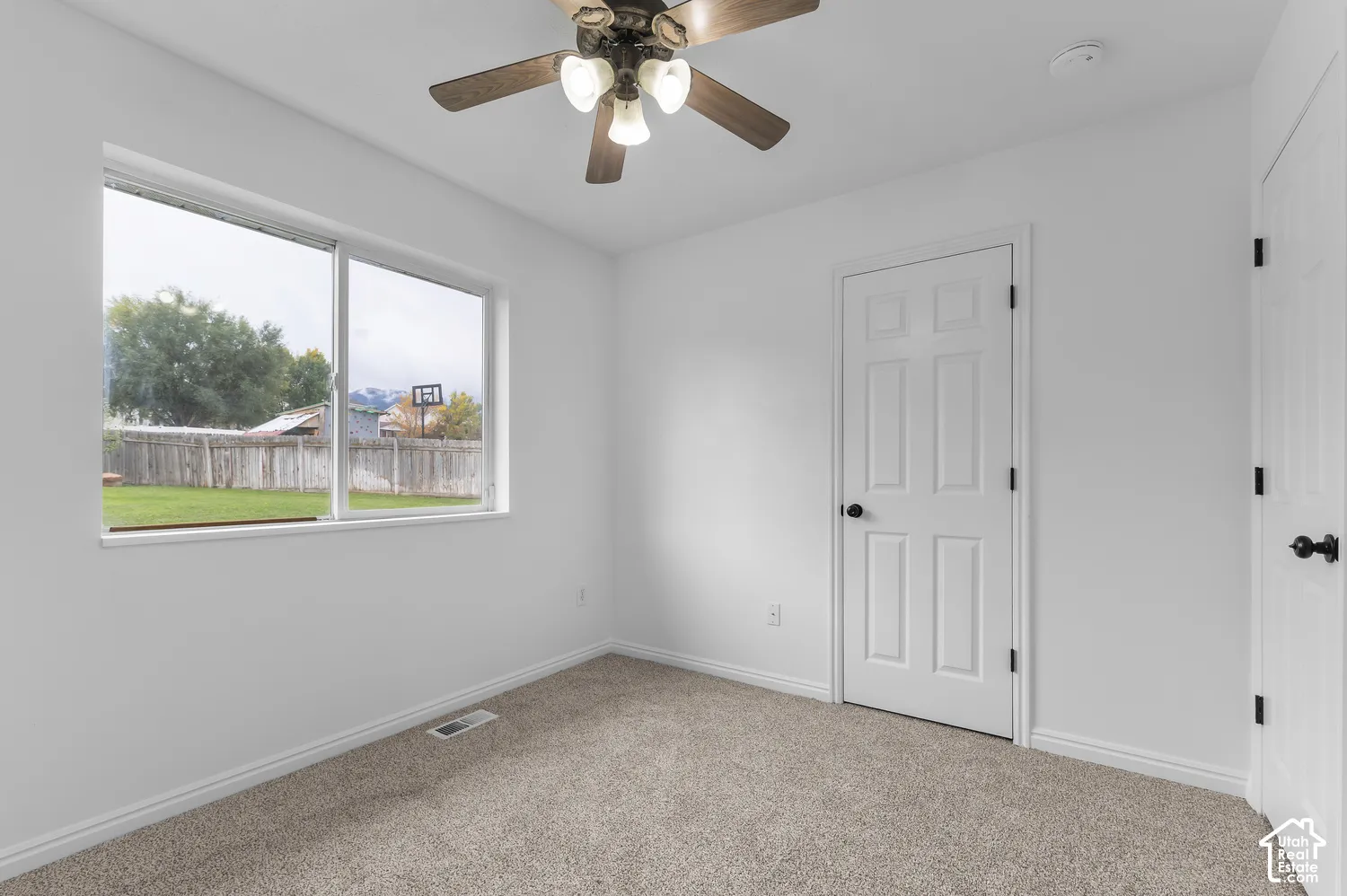 Neutral-toned carpeting, white walls, six-panel interior doors with matte black hardware, and a ceiling fan with integrated lighting