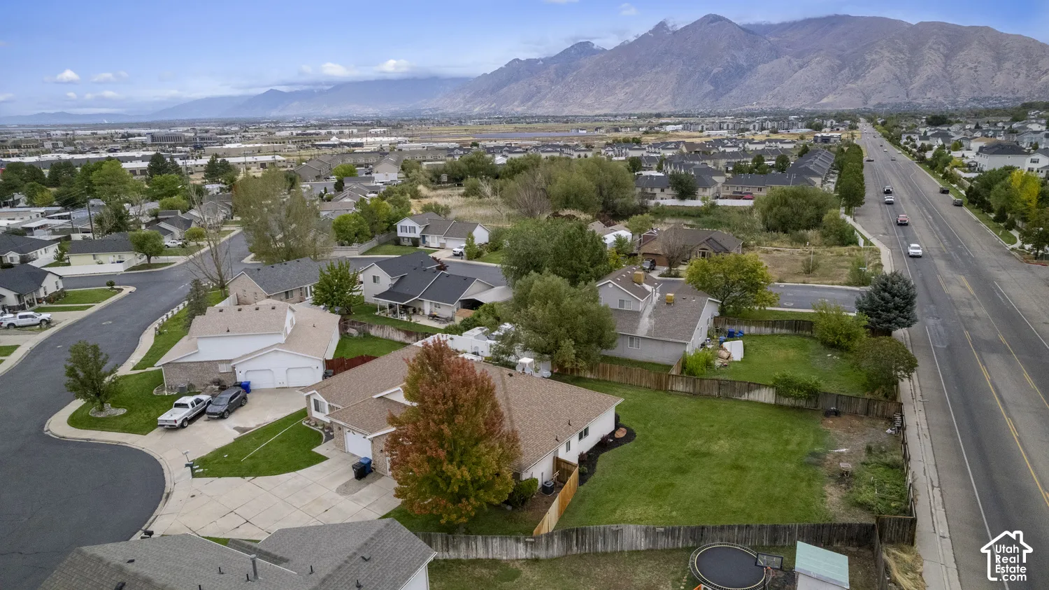 Aerial perspective featuring an expansive lawn, concrete driveway, attached  garage, mature landscaping, and prominent mountain backdrop