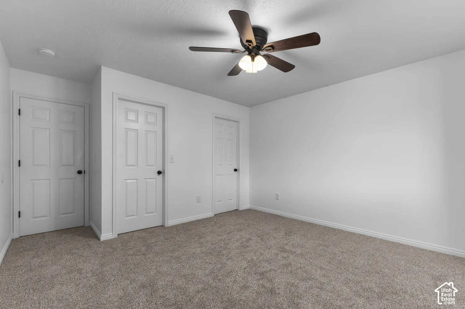 Neutral-toned wall-to-wall carpeting, three six-panel interior doors, and a ceiling fan with integrated light fixture