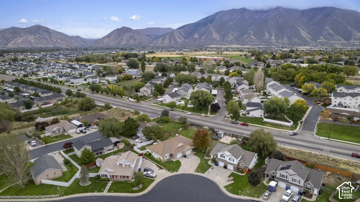Aerial perspective of a residential neighborhood featuring expansive mountain backdrops, paved cul-de-sac streets, mature trees, and landscaped yards