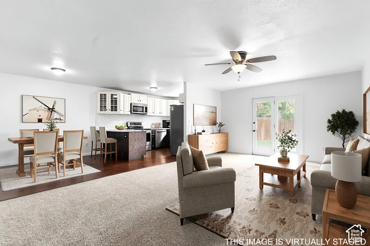 Open-concept area featuring white cabinetry, subway tile backsplash, dark-toned kitchen island, wood-finish flooring, and glass-paneled exterior door