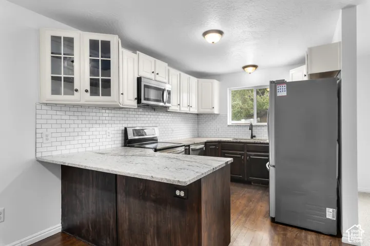 Kitchen featuring two-tone cabinetry, stone-finish countertops, subway tile backsplash, stainless steel appliances, and wood-finish flooring