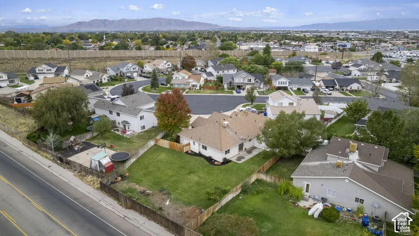 Aerial perspective of a residential property featuring a fenced backyard, manicured lawn, mature trees, and a mountain range backdrop