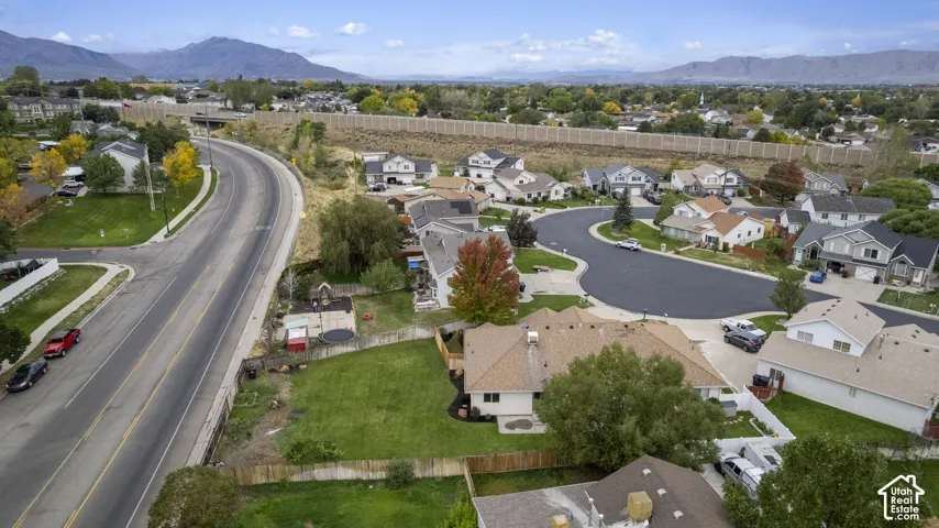 Aerial perspective of a residential property featuring an expansive grass lawn, wood-panel fencing, a multi-pitch shingled roof, and a mountain backdrop
