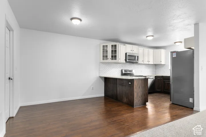 Kitchen featuring two-tone cabinetry, wood-finish flooring, white subway tile backsplash, stone-surface countertop, and stainless steel built-in appliances