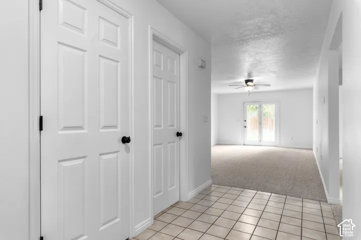 Ceramic tile flooring, six-panel interior doors with matte black hardware, neutral-toned carpeting, ceiling fan with integrated lighting, and full-glass paneled French doors