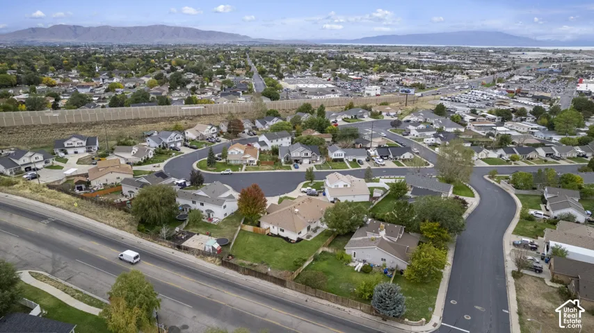 Aerial perspective of the residential area featuring asphalt streets, manicured green space, mature trees, and a mountain range backdrop