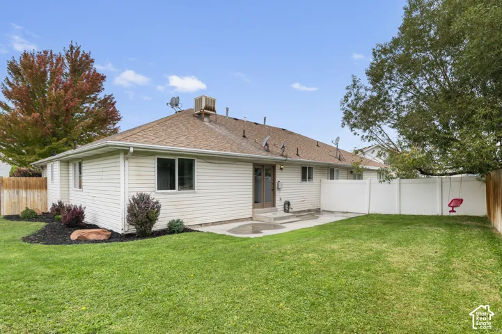 Exterior elevation featuring light-toned horizontal siding, a composition shingle roof, a concrete patio, and white vinyl perimeter fencing