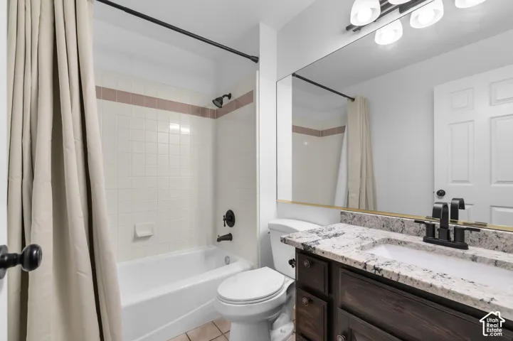 Bathroom featuring stone-finish countertop, dark wood-finish cabinetry, matte black hardware, full-width wall mirror, and a tiled shower surround