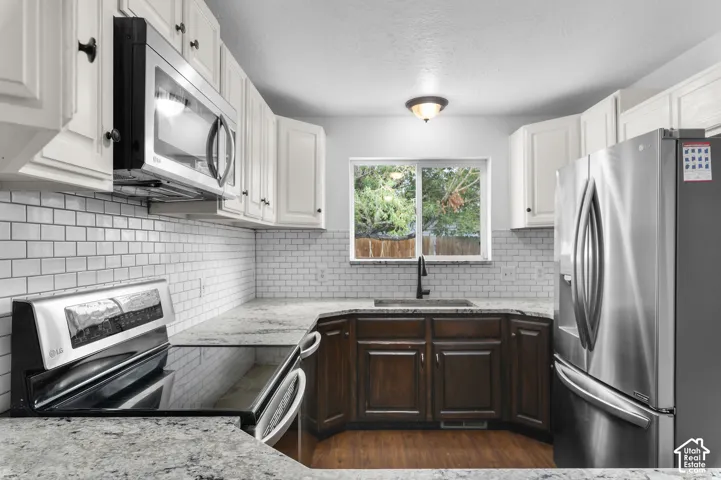 Kitchen featuring stone countertops, white subway tile backsplash, stainless steel appliances, dual-tone cabinetry, and wood-finish flooring