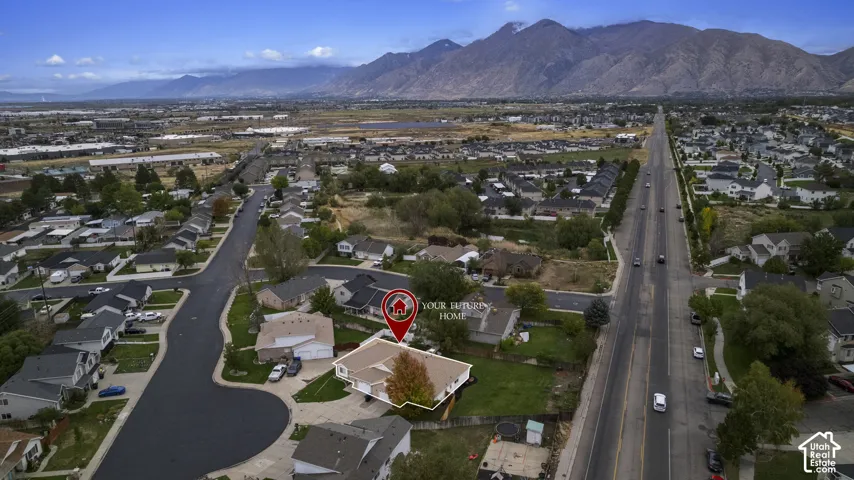 Aerial perspective featuring a single-story residence with a multi-gabled roof, integrated garage, and fenced backyard, situated against a backdrop of mountain scenery