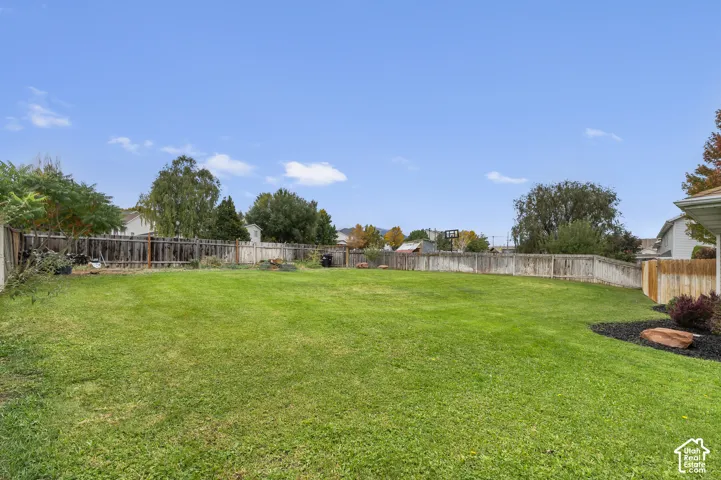 Expansive backyard featuring a large grass lawn, full-perimeter wood fencing, and landscaped garden beds with stone accents