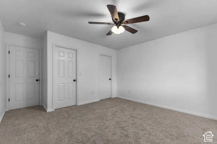Neutral-toned wall-to-wall carpeting, three six-panel interior doors, and a ceiling fan with integrated light fixture