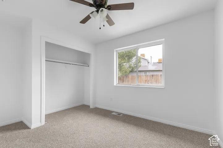 Neutral-toned carpeting, ceiling fan with integrated light fixture, and walk-in closet featuring a built-in rod