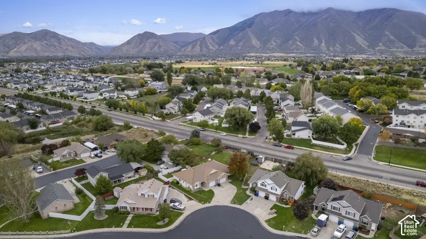 Aerial perspective of a residential neighborhood featuring expansive mountain backdrops, paved cul-de-sac streets, mature trees, and landscaped yards