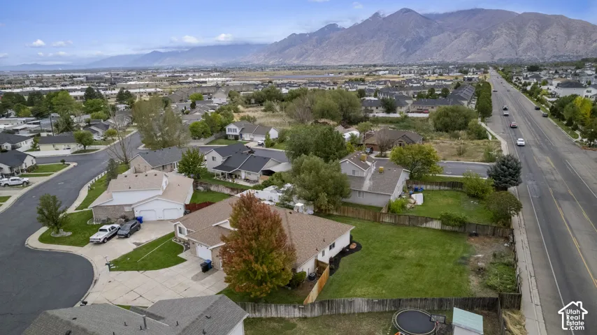 Aerial perspective featuring an expansive lawn, concrete driveway, attached  garage, mature landscaping, and prominent mountain backdrop