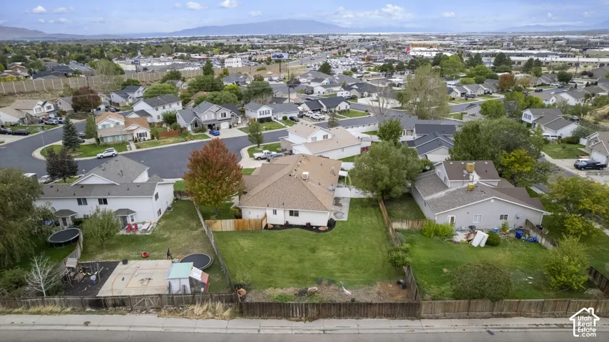 Aerial view of a residential lot featuring a manicured lawn, perimeter wood fencing, and mature trees against a mountain backdrop