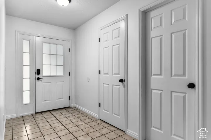 Entryway featuring ceramic tile flooring, a six-pane glass window door with a matching side light, and six-panel interior doors with matte black hardware