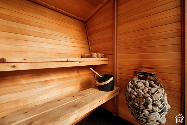 Wood-paneled sauna featuring a built-in heater with natural stones and two tiered benches