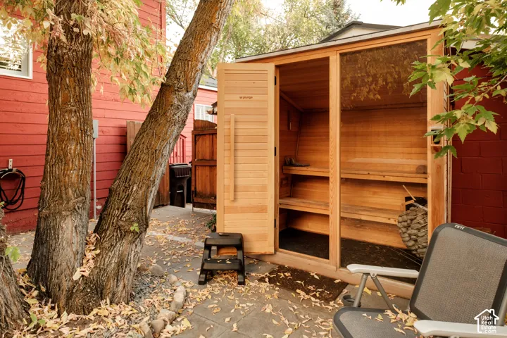 Outdoor sauna with wood paneling, multiple interior benches, and a visible heater with stones, set on a stone paver patio
