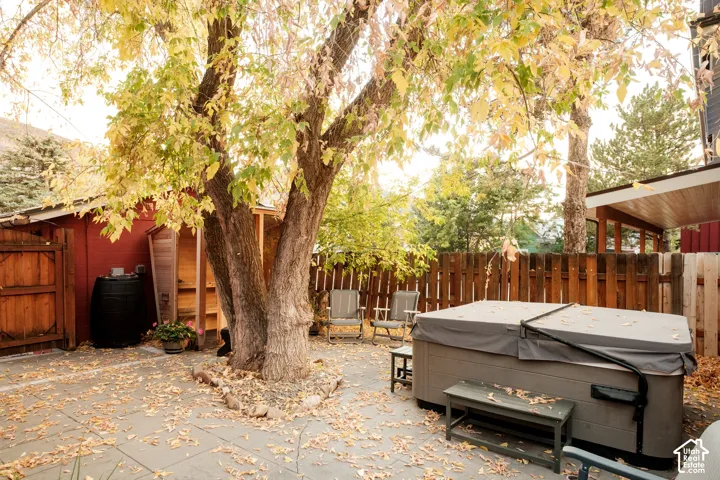 Paved patio with mature trees, wooden privacy fencing, and a covered hot tub