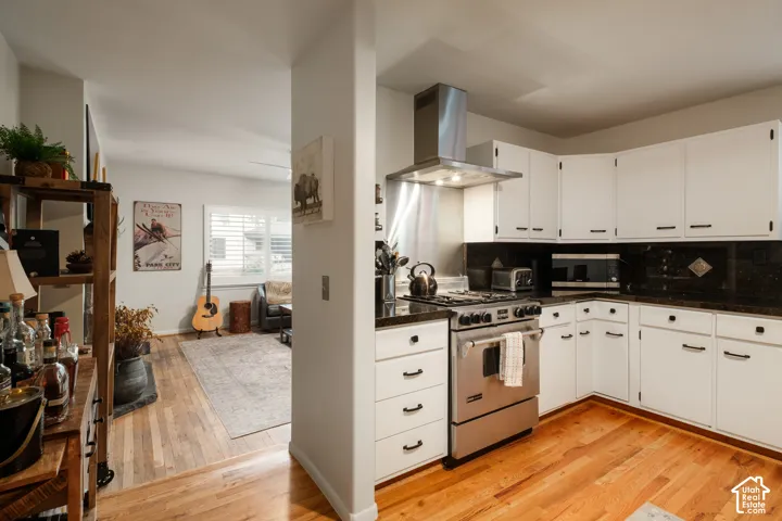 Kitchen featuring white cabinetry, dark countertops, stainless steel gas range, and a stainless steel range hood
