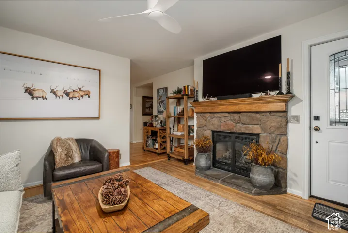 Stone fireplace with a wood mantle, wood-finish flooring, white ceiling fan, and decorative glass entry door
