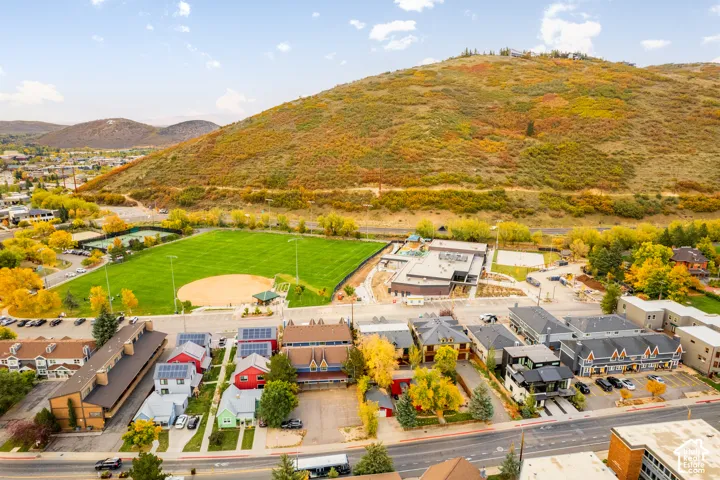 Expansive mountain backdrop with varied foliage, bordering a large athletic field, tennis courts, and urban development