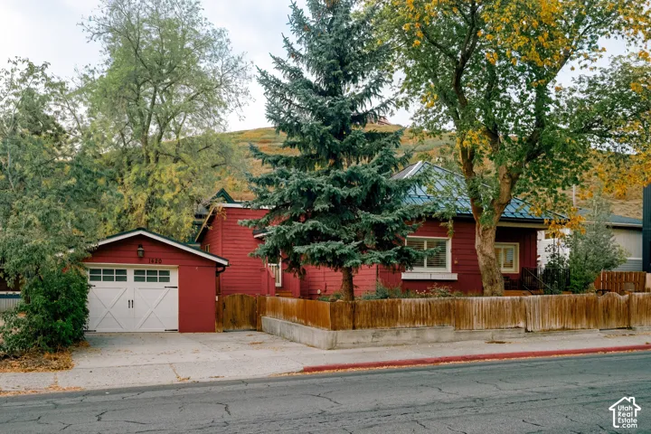 Red exterior siding with white trim, attached garage with carriage-style door, paved driveway, wood fencing, and mature trees