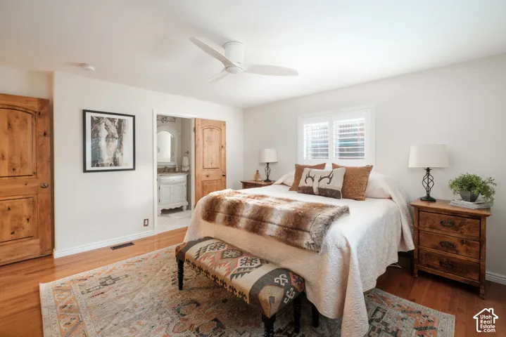 Hardwood flooring, wood panel doors, ceiling fan, window with plantation shutters, and an attached bathroom with a single vanity