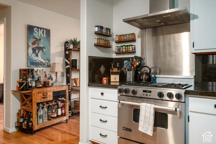Stainless steel range with a built-in hood, dark stone countertops, and white cabinetry with dark hardware