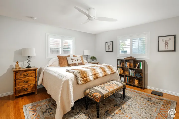 Hardwood flooring, two windows with white plantation shutters, a ceiling fan, and light-toned walls
