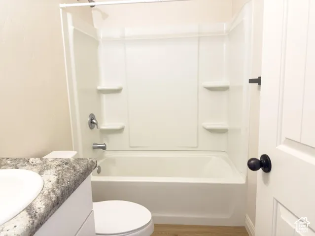 Bathroom featuring a white molded tub-and-shower surround with integrated shelving, stone-patterned vanity countertop, white cabinet base, and matte black hardware