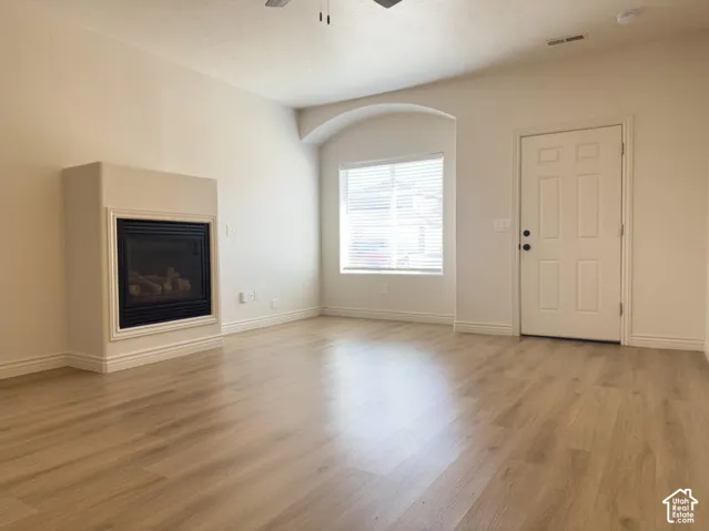 Living area featuring wood-finish flooring, a fireplace with a minimalist surround, an arched window alcove, and a six-panel door