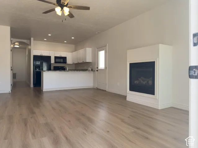 Open-concept interior featuring wood-finish flooring, a wall-mounted fireplace with a custom surround, white cabinetry, an eat-in peninsula counter, and recessed lighting