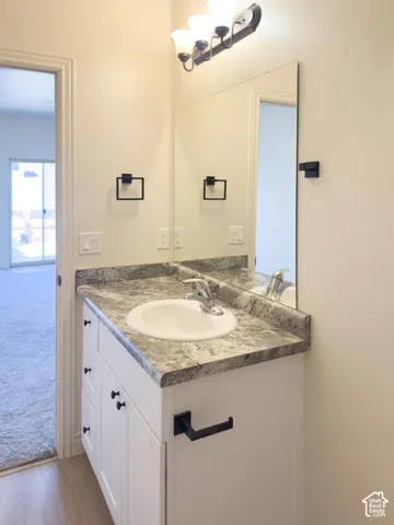 White vanity with stone-patterned countertop, integrated basin, matte black hardware, wall-mounted mirror, and three-light fixture