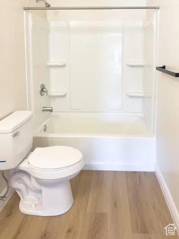Full-height white tub surround with integrated shelving, chrome shower hardware, porcelain toilet, and wood-finish flooring