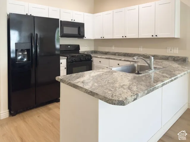 Kitchen featuring white shaker-style cabinetry, stone-patterned countertops, stainless steel sink, wood-finish flooring, and black appliances