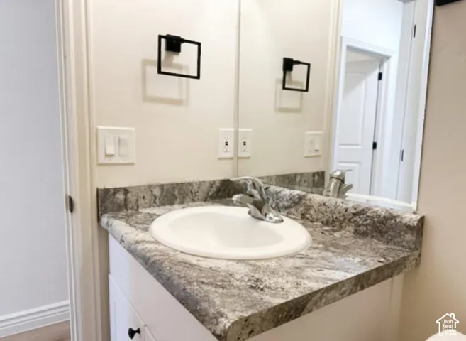 Vanity featuring a stone-patterned countertop, integrated oval sink, chrome faucet, matte black towel ring, and mirror with an integrated light fixture